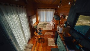 A cozy cabin interior with a wooden floor, a bed with a canopy, a dining area with a table and chairs, a kitchenette, and a television.