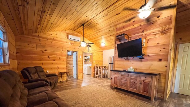 A log cabin interior with a sofa, TV, and wooden cabinets.