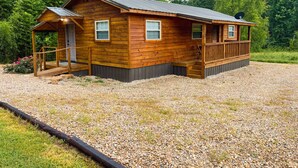 A wooden cabin with a porch, a satellite dish, and a gravel driveway.