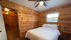 A wooden-paneled bedroom with a bed, a window, a ceiling fan, and a nightstand.