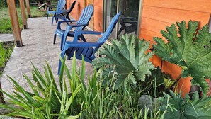 Une cabane en bois dotée d’un patio couvert, avec des chaises Adirondack bleues et un chemin en pierre.