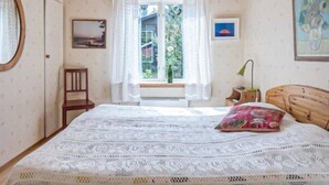 A bedroom with a bed, a window with curtains, a chair, a bedside table with a lamp, and a framed picture on the wall. - Awesome home in Linneryd with lake view (Linneryd)