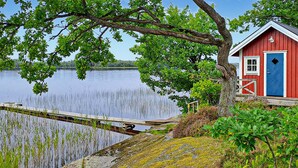 A red and blue cabin by a calm lake with a dock extending into the water. - Awesome home in Linneryd with lake view (Linneryd)