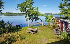 A lakeside cabin with a picnic table and a dock extending into the water. - Awesome home in Linneryd with lake view (Linneryd)