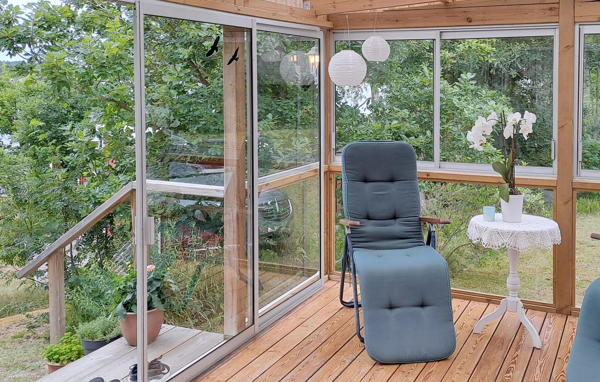 A conservatory with a cushioned chair, a small table with a potted orchid, and a view of lush greenery.