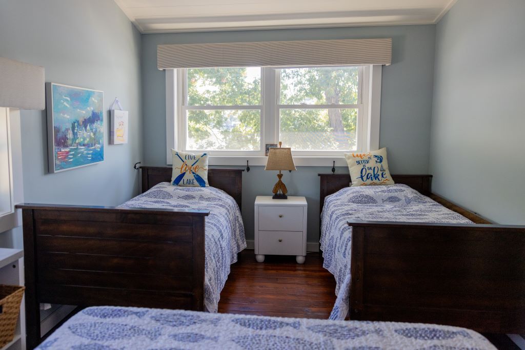 Une chambre à coucher avec deux lits en bois, une table de chevet, une fenêtre donnant sur des arbres et un tableau accroché au mur.