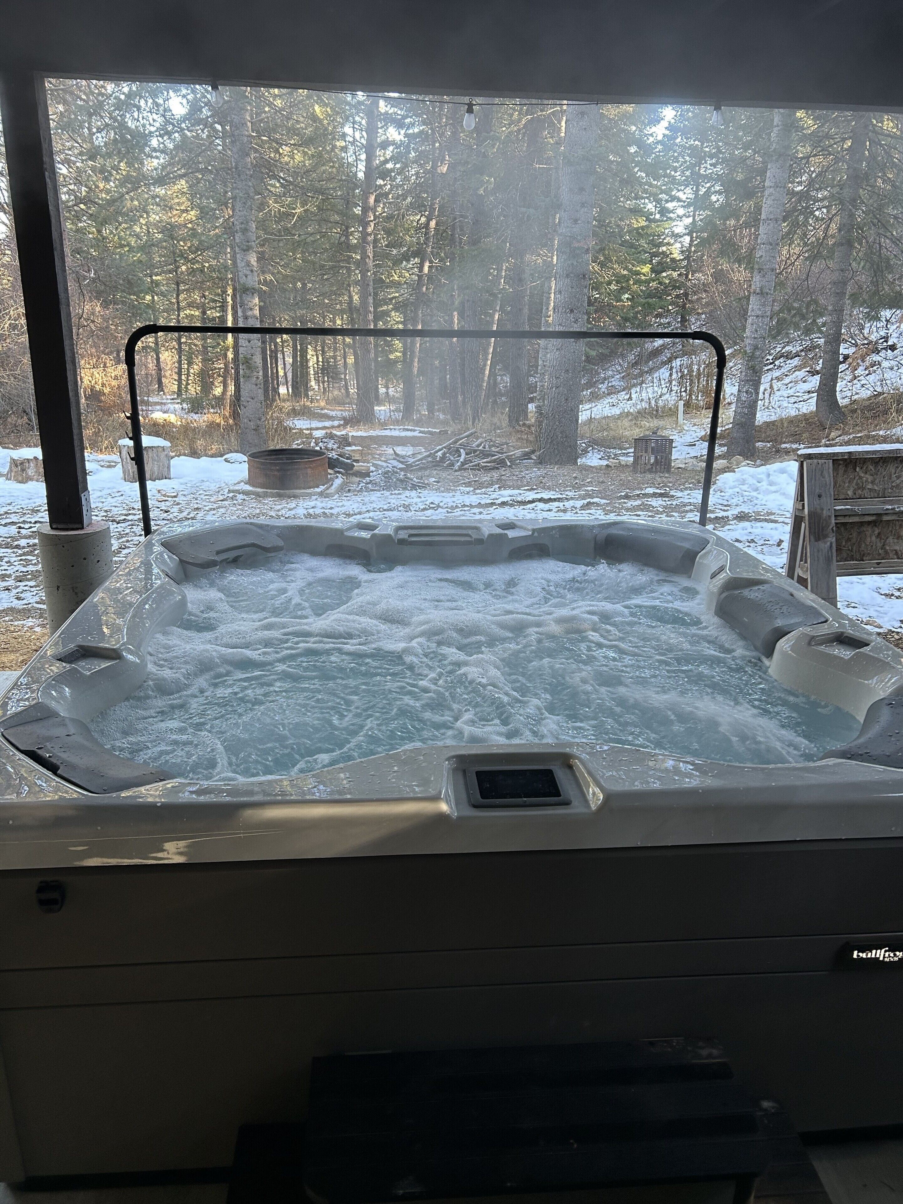 A hot tub with a metal frame and a view of a forested area with trees and a wooden structure in the background.