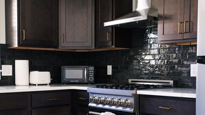 A modern kitchen with dark wood cabinets, a stainless steel range hood, a microwave, and a built-in oven. - The Mane & Co - No. 8 (Chambersburg)