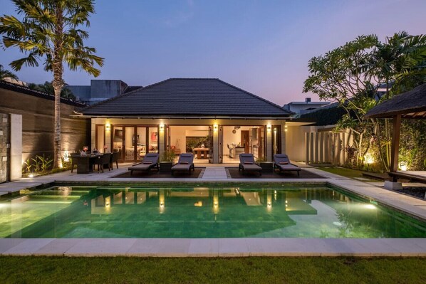 A modern house with a swimming pool, outdoor seating, and a well-lit patio area.
