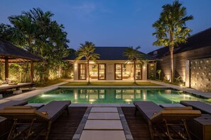 A poolside area with lounge chairs, a swimming pool, and a building with large windows and a stone facade.
