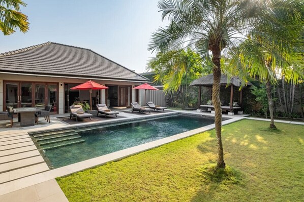 A modern house with a swimming pool, outdoor seating, and palm trees.