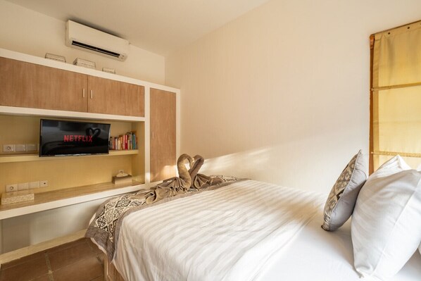 A hotel room with a bed, a TV, a bookshelf, and a window with curtains.