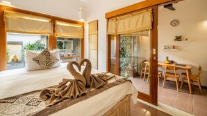 A bedroom with a bed, a heart-shaped towel, a dining area with a table and chairs, and a view of a garden through a sliding door. - Villa private Pool in Seminyak, Car Park fast WIFI (seminyak)