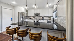 A modern kitchen with white cabinets, a large island with bar stools, stainless steel appliances, and pendant lighting. - San Diego City Escape – Perfect for Families, Groups, & Business Travelers (San Diego)
