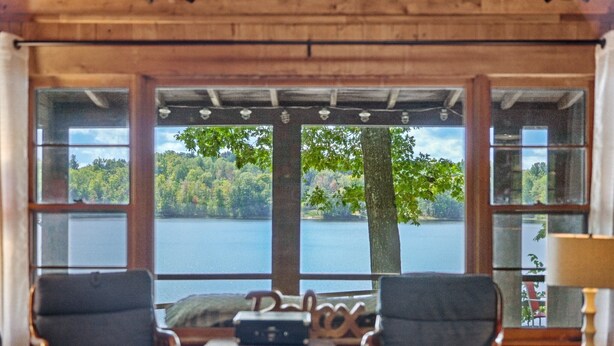 Ein Zimmer mit zwei Sesseln vor einem großen Fenster mit Blick auf einen See und Wald.