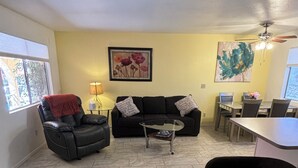 A living room with a black leather sofa, a coffee table, a dining table with chairs, and a ceiling fan.