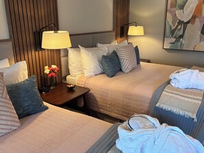 A hotel room with two beds, a nightstand with a vase of flowers, two wall-mounted lamps, and a painting on the wall.