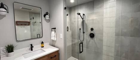A modern bathroom with a glass-enclosed shower, a white sink, and a mirror above it.