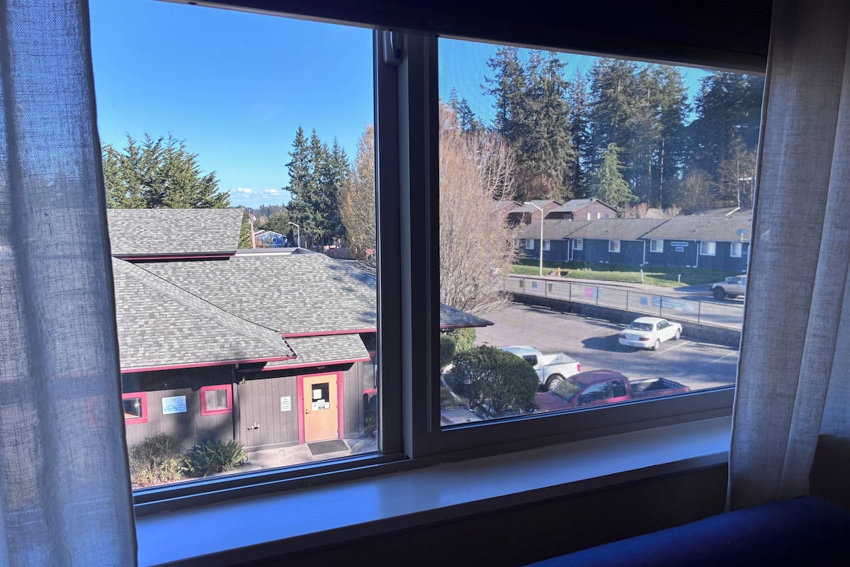 A window with a view of a building with a red door and a parking lot.