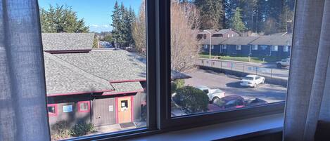 A window with a view of a building with a red door and a parking lot.