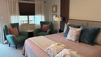 A hotel room with a bed, two armchairs, a small table, a lamp, and a window with curtains.
