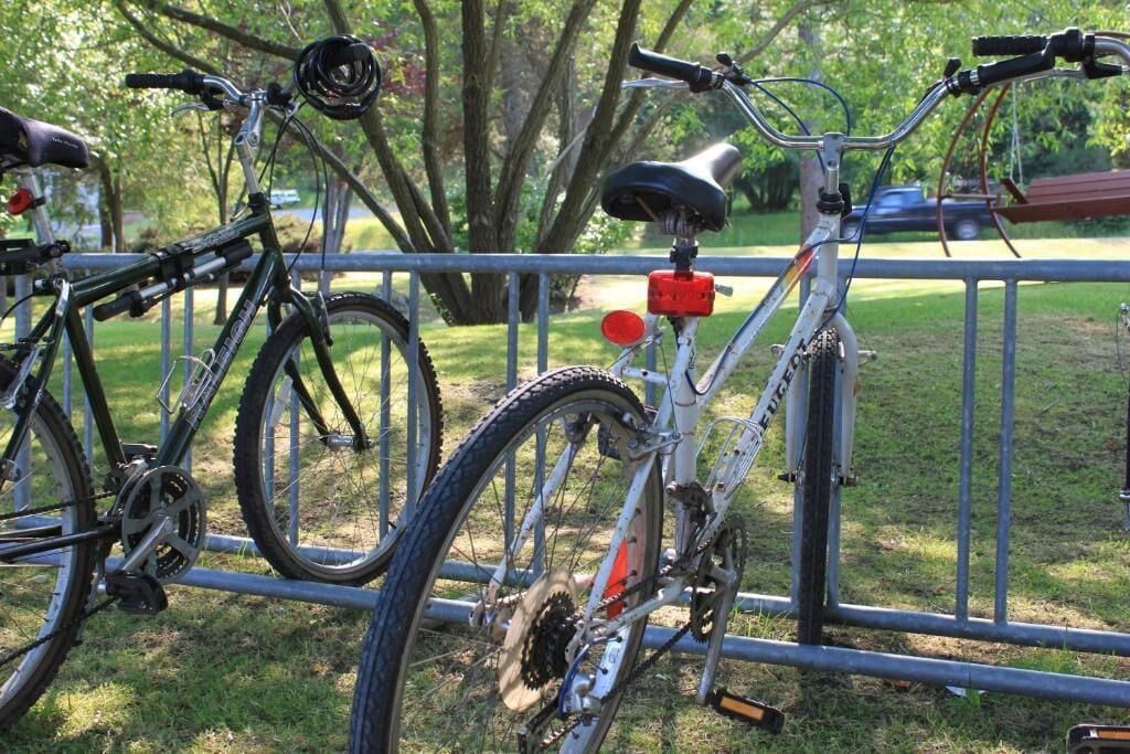 A bicycle secured to a metal fence in a grassy area with trees in the background.
