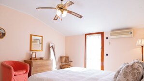 Un dormitorio con cama, una silla, cómoda, espejo, ventilador de techo y aire acondicionado.