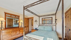 Un letto a baldacchino con testiera in legno, una cassettiera di legno con cassetti, uno specchio e un comodino con una lampada.