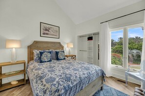 A bedroom with a large bed, two bedside tables, a wardrobe, and a window with a view of greenery. - Stella Maris-Beautiful Deluxe Home w/ Private Pool & Ocean Views;Across from Beach Access (Edisto Beach)