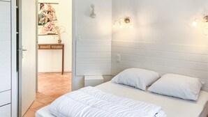 Ett sovrum med en säng, ett sängbord, en väggmonterad lampa och en dörr som leder till ett annat rum.