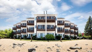 Un immeuble à plusieurs étages doté de balcons, situé dans une zone sablonneuse parsemée de rochers.