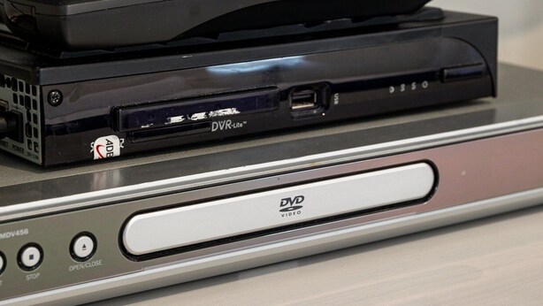 A DVD player with a remote control on top, placed on a shelf. - Bayfront Bliss at the Beaches (Traverse City)