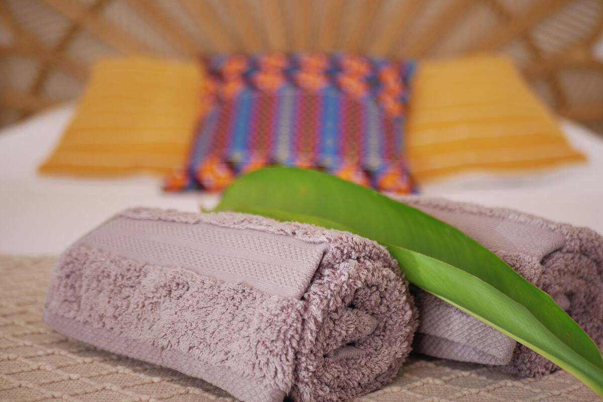 Una cama bien hecha con una toalla enrollada y una hoja verde encima.
