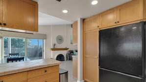 Una cocina con gabinetes de madera, un refrigerador negro y una ventana que da a un patio trasero.