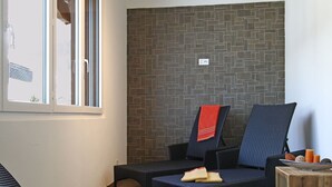 Una habitación con dos sillones de mimbre, una mesita de madera y un muro de azulejos con un diseño geométrico.