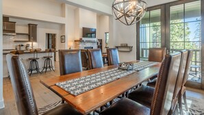 A spacious dining area with a long wooden table, leather chairs, and a geometric pendant light.