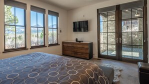 A bedroom with a large bed, a dresser, a TV mounted on the wall, and a sliding glass door leading to an outdoor area.