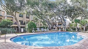 Ein Pool mit Liegestühlen, umgeben von Bäumen und einem Pflasterweg.