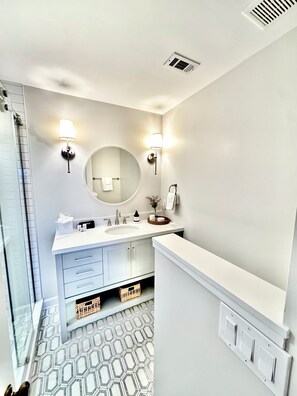 Un baño moderno con un tocador blanco, un espejo redondo y dos luces empotradas.