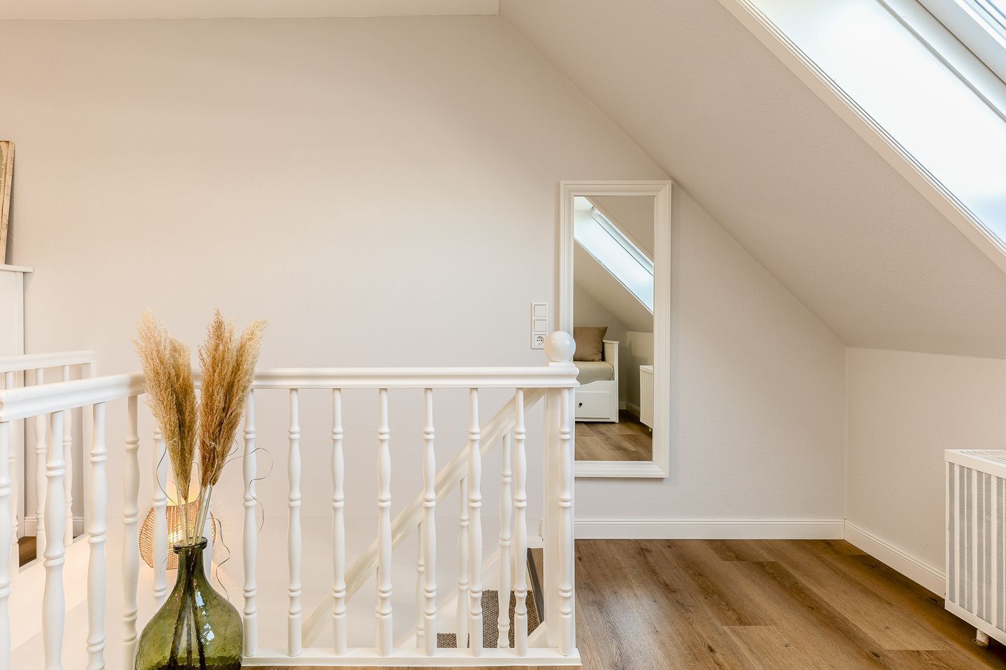 Une pièce avec un escalier blanc, un plancher en bois et une lucarne.