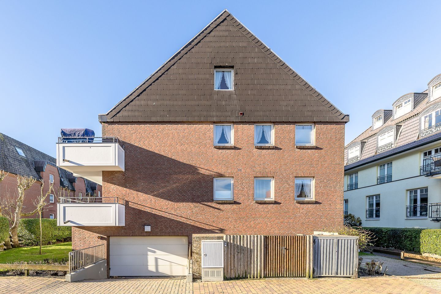 Ein zweistöckiges Wohngebäude mit Schrägdach, mehreren Fenstern, einer Garage und einem umzäunten Garten.