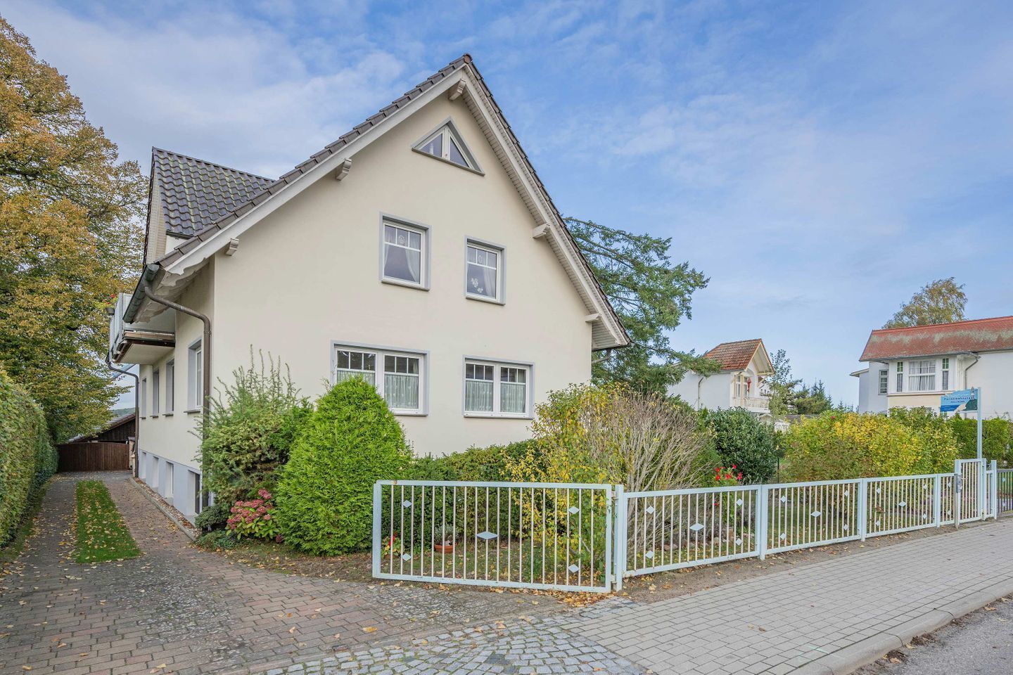 A two-story house with a sloped roof, a front garden, and a paved driveway.