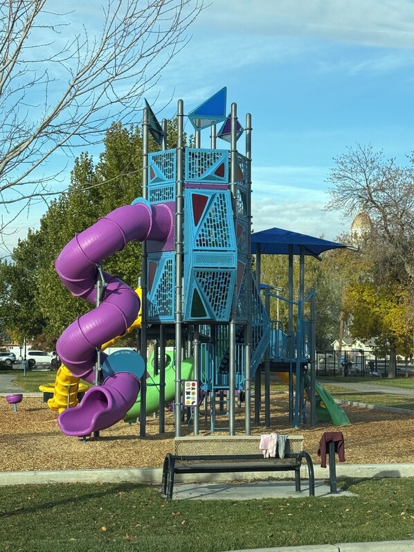 Une aire de jeux avec un toboggan violet, un toboggan vert et une structure d’escalade bleue.