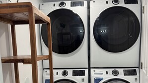Un cuarto de lavandería con cuatro lavadoras de carga frontal apiladas y un estante de madera.