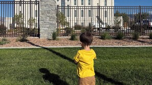 Un niño parado en una acera frente a un edificio grande con una torre y una cúpula destacadas.