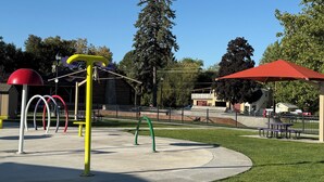 Un parque infantil con columpios, toboganes y un pabellón de techo rojo.