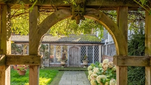A wooden pergola structure with a stone pathway leading to a traditional building with a tiled roof. - Splendid 1,000 year old Medieval manor house  sleeps up to 14 or 22- Flemings Hall (Ipswich)