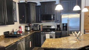 Una cocina moderna con armarios oscuros, electrodomésticos de acero inoxidable, encimeras de granito e iluminación colgante.