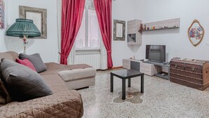 A living room with a sofa, a small table, a television, a cabinet, and a window with curtains. - GuestHost - Comfy APT in Genoa's St. Theodore District (Genova)