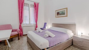 A bedroom with a bed, a chair, a table, and a window with curtains. - GuestHost - Comfy APT in Genoa's St. Theodore District (Genova)